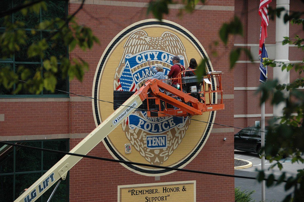 A man in a jlg lift is painting a police seal on a brick building