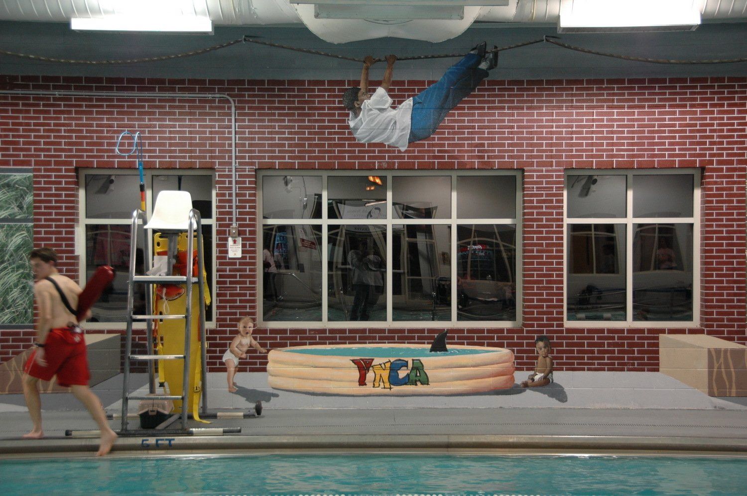 A man is hanging from the ceiling of a swimming pool.