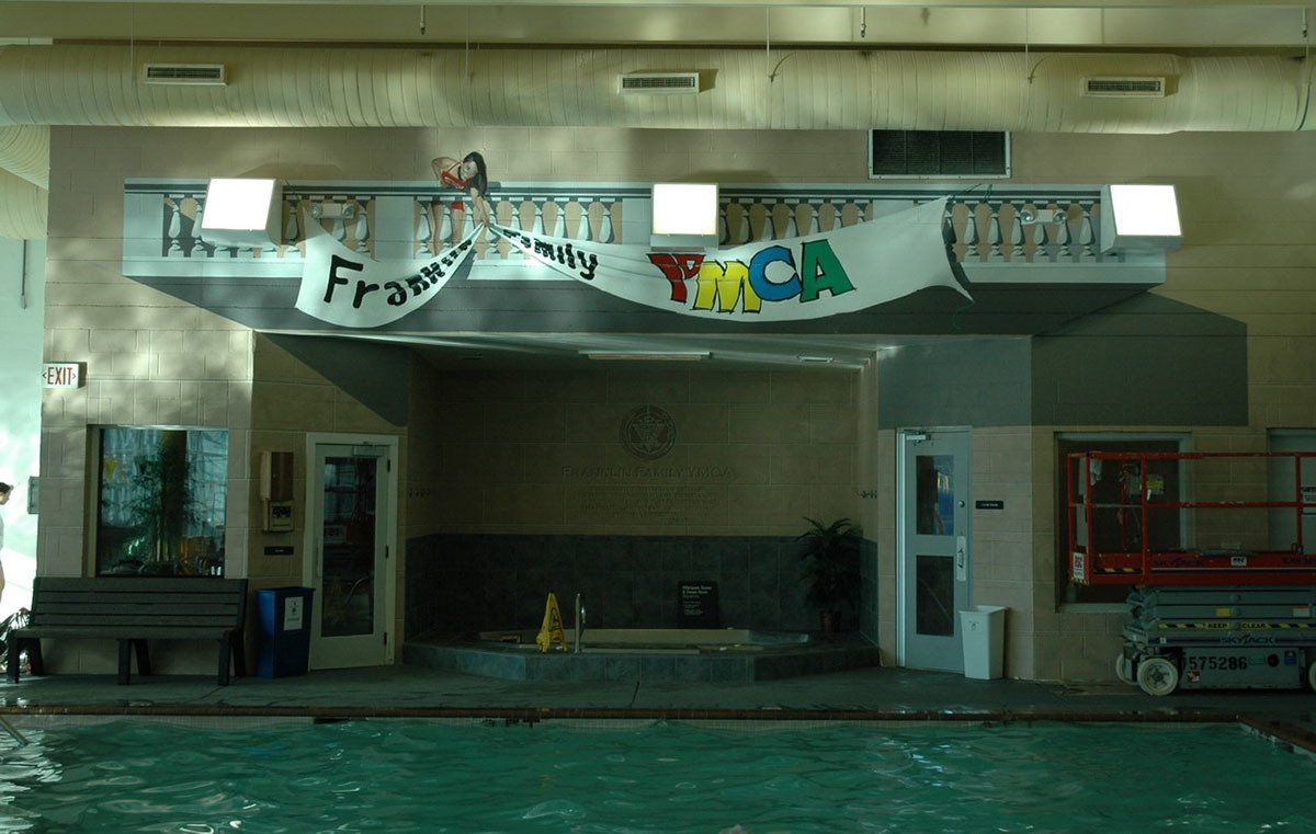 A large indoor swimming pool with a banner hanging from the ceiling that says tmca