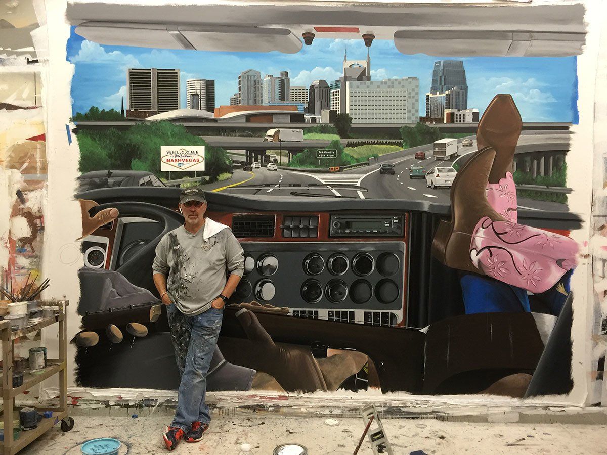 A man is standing in front of a painting of a truck dashboard.