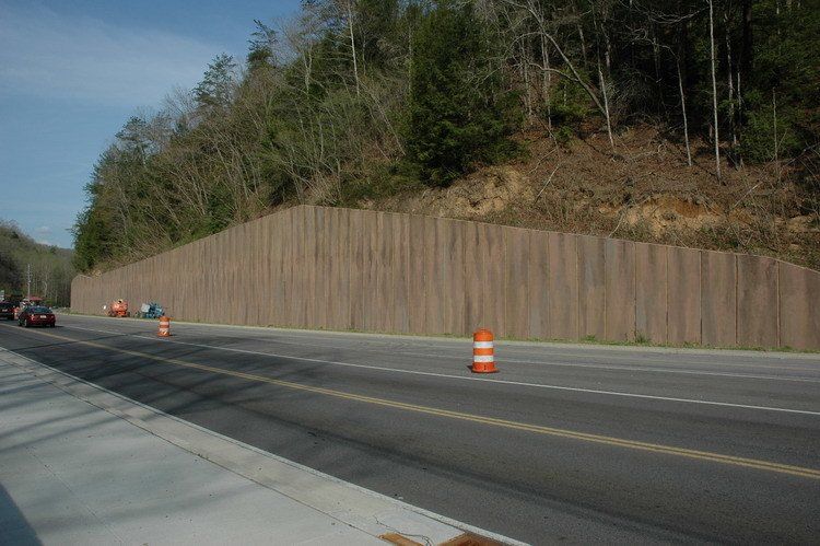 A car is driving down a highway next to a wooden wall.