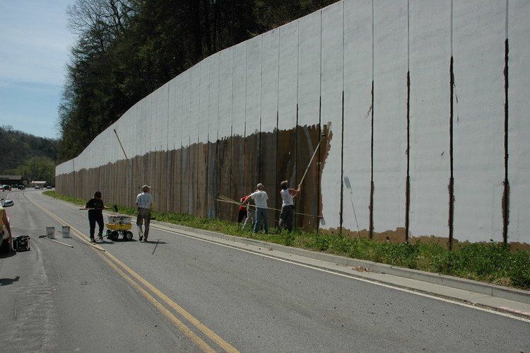 A group of people are painting a wall on the side of a road