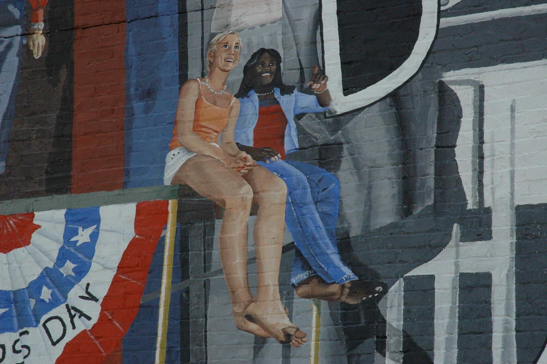 Two women are sitting on a railing in front of a banner that says us day