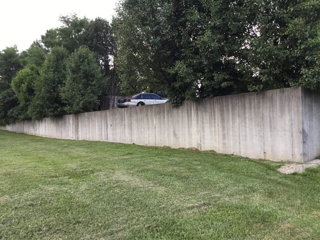 A concrete fence surrounds a grassy field with trees in the background.