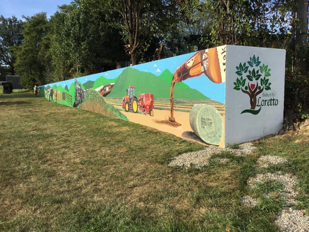 A wall with a painting of a woman pouring a drink into a tree.