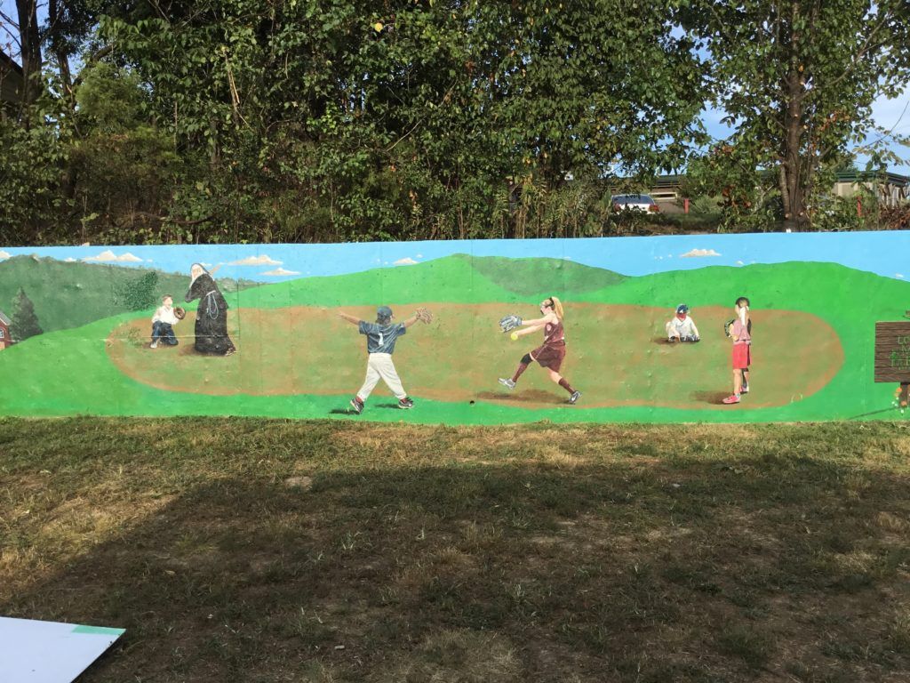 A mural of baseball players on a field with trees in the background.