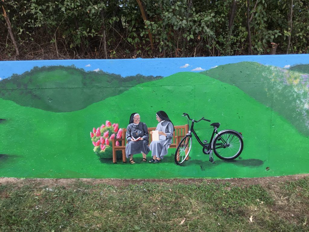 A painting of two women sitting on a bench next to a bicycle