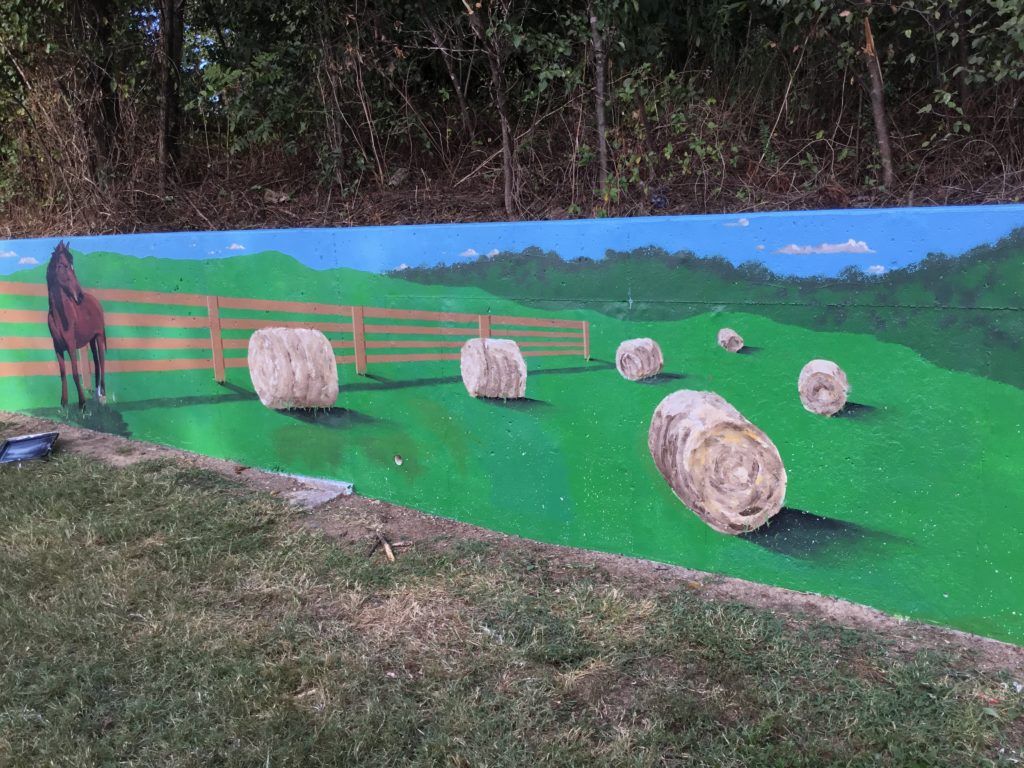 A painting of a horse and hay bales on a wall.