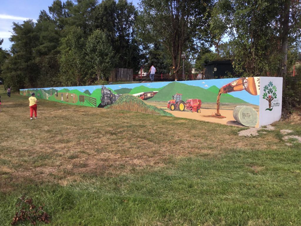 A painting of a tractor is on a wall in a field.