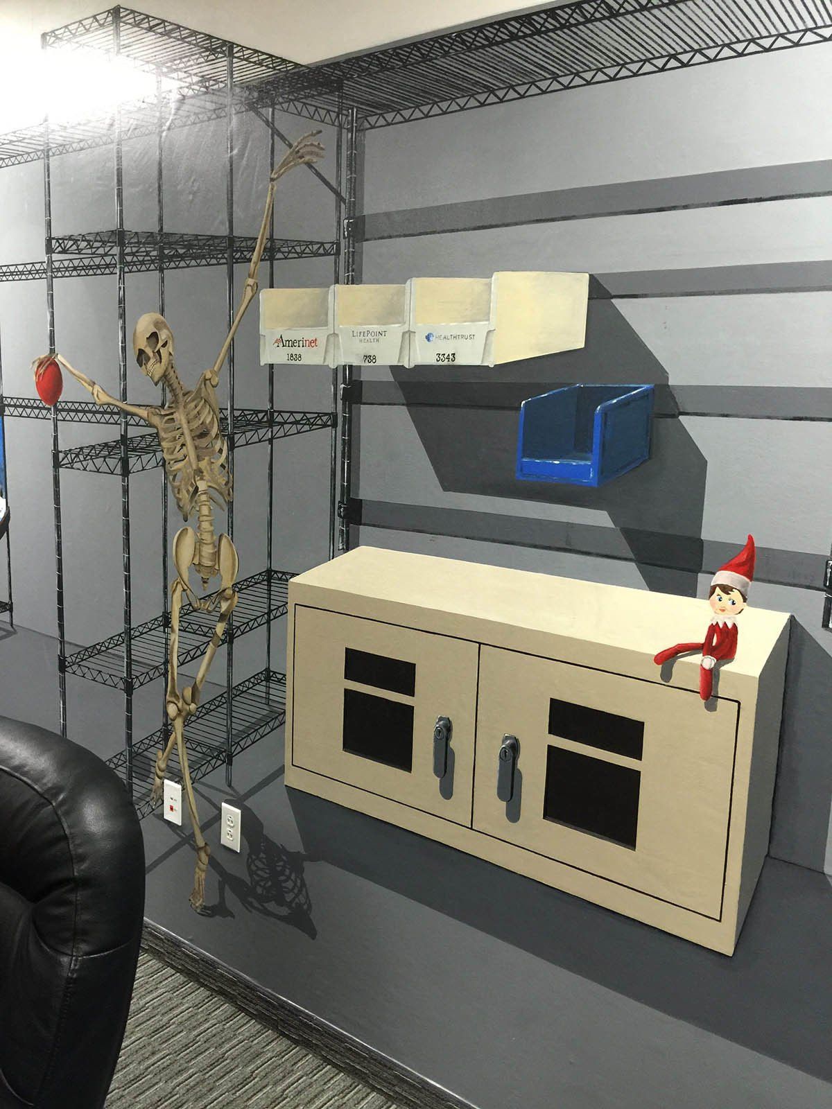 A skeleton is standing next to an elf on the shelf in a room.