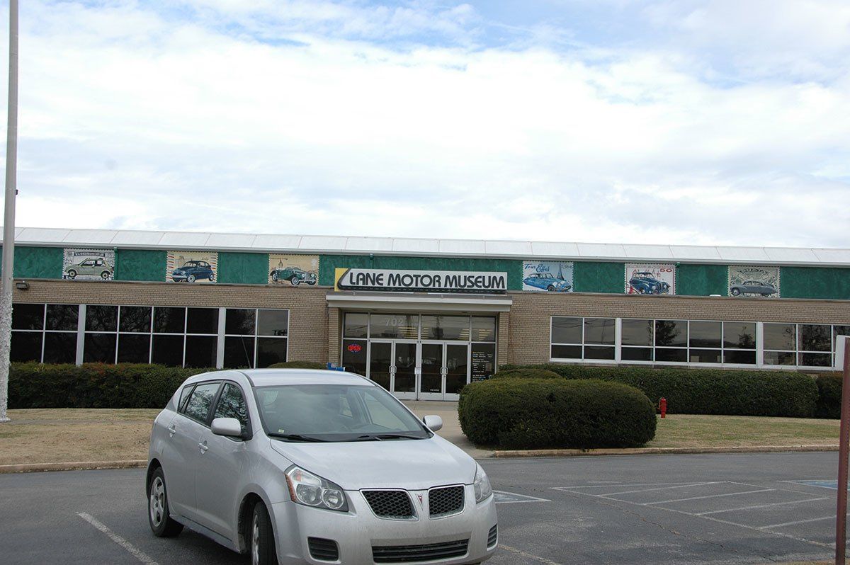 A silver car is parked in front of a large building.