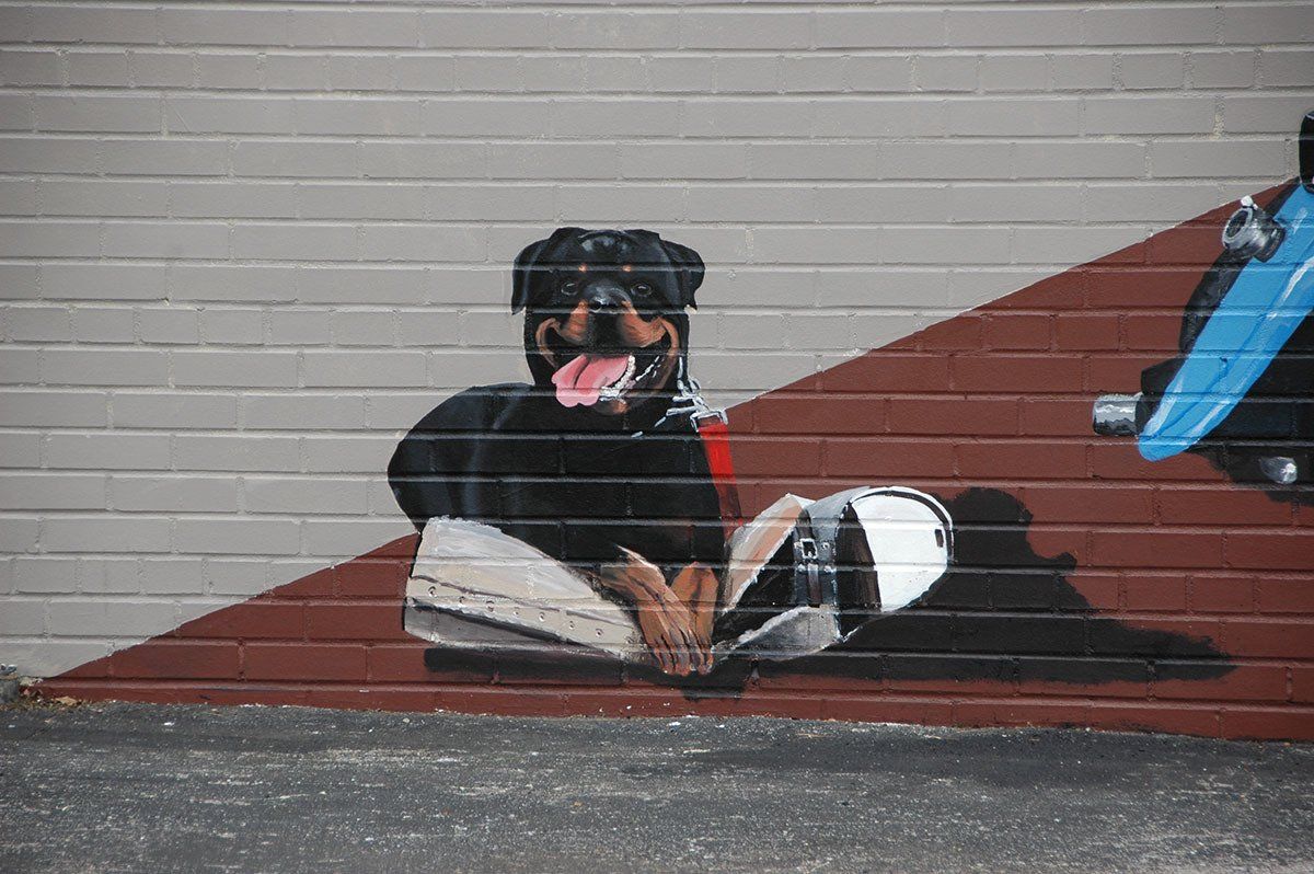 A mural of a dog reading a book on a brick wall.