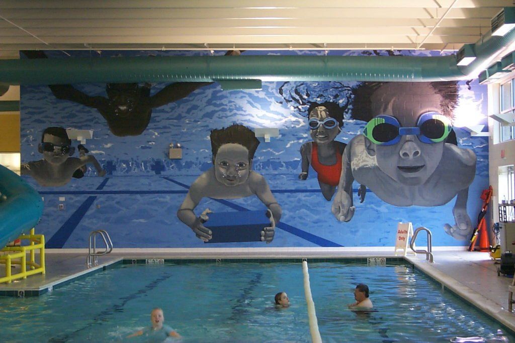 A group of people are swimming in a large indoor swimming pool.