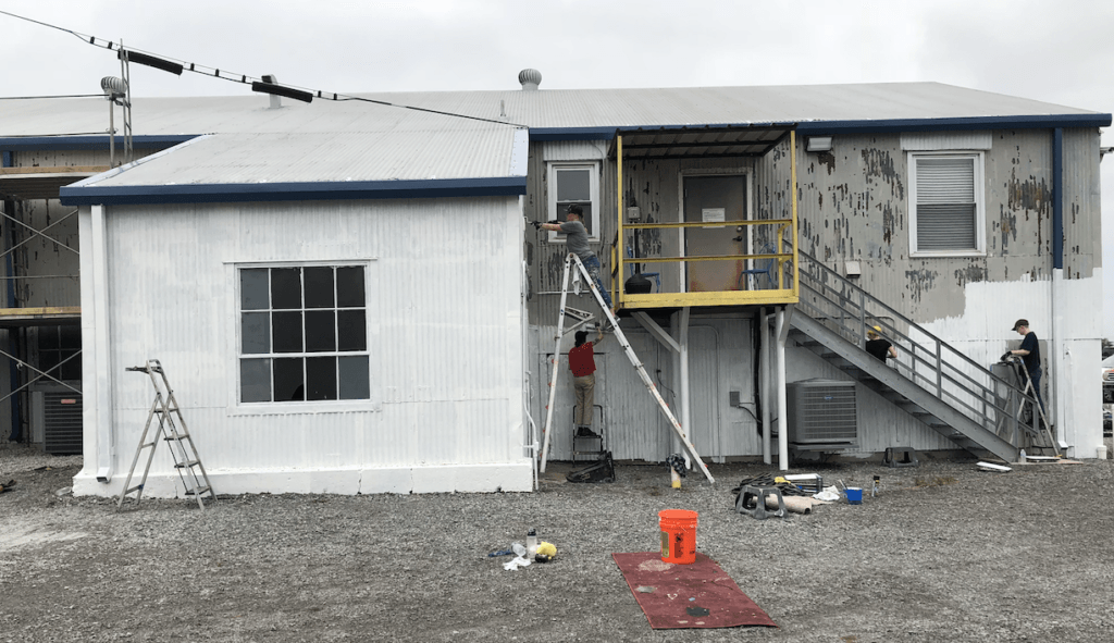 A man is painting the side of a building with a ladder.