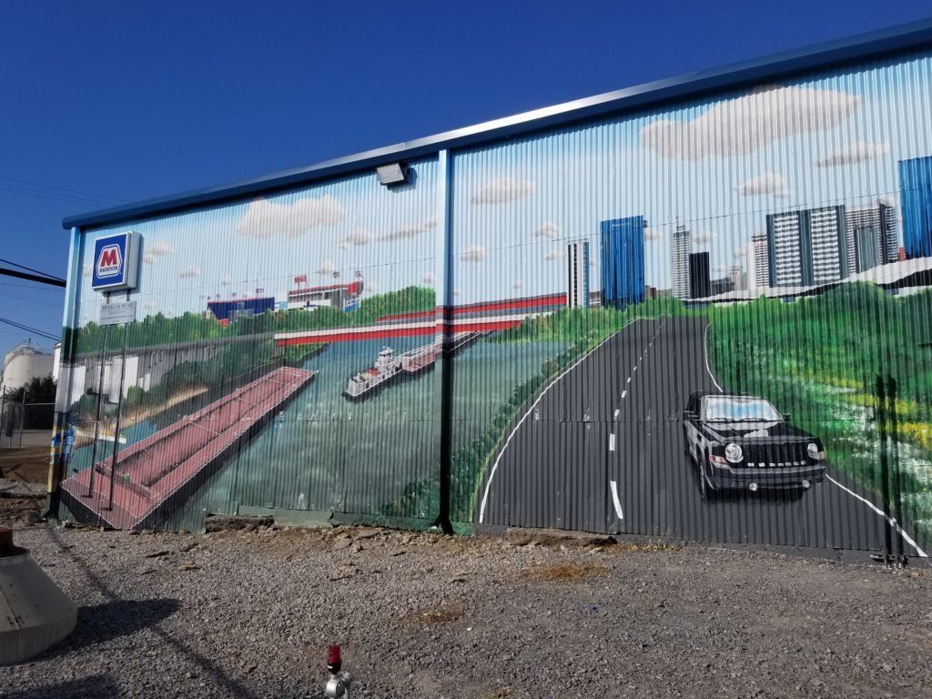 A large mural on the side of a building shows a car driving down a road.
