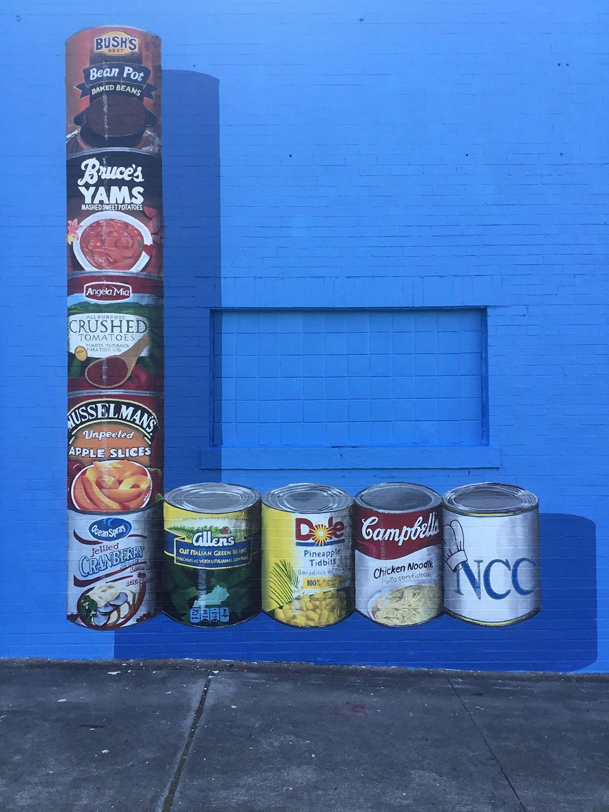 A row of cans of food are stacked on top of each other on a blue wall.