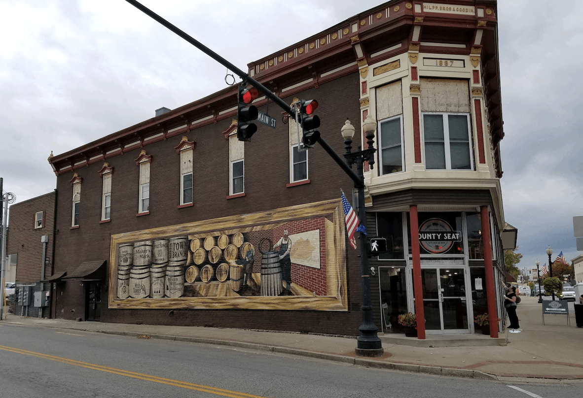 A brick building with a mural on the side of it is on the corner of a street.
