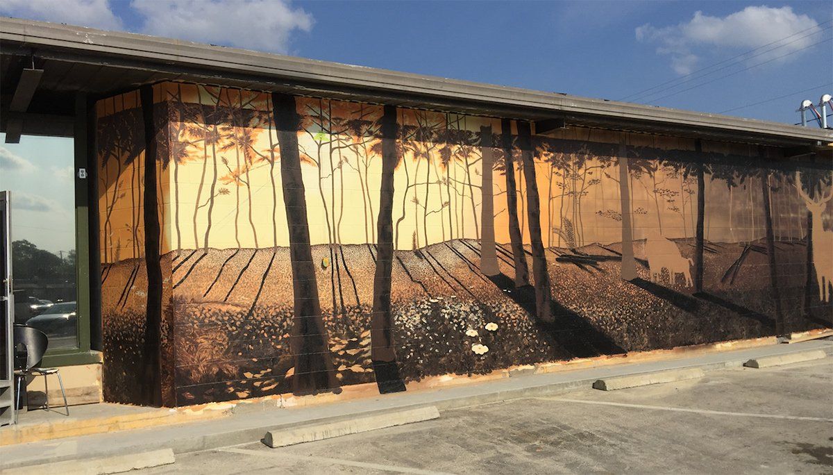 A large painting of trees on the side of a building in a parking lot.