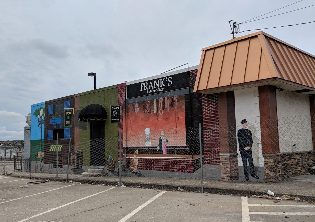 A building with a mural on the side of it and a parking lot in front of it.