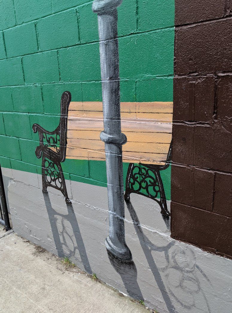 A painting of a bench and a lamp post on a brick wall