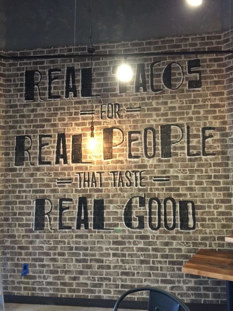 A brick wall with a quote on it that says real tacos for real people that taste real good