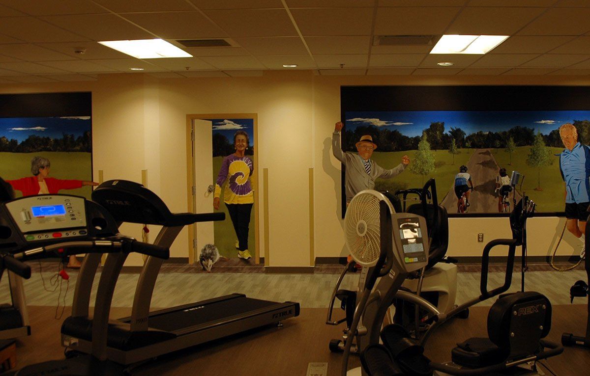 A gym with treadmills , exercise bikes and a mural on the wall
