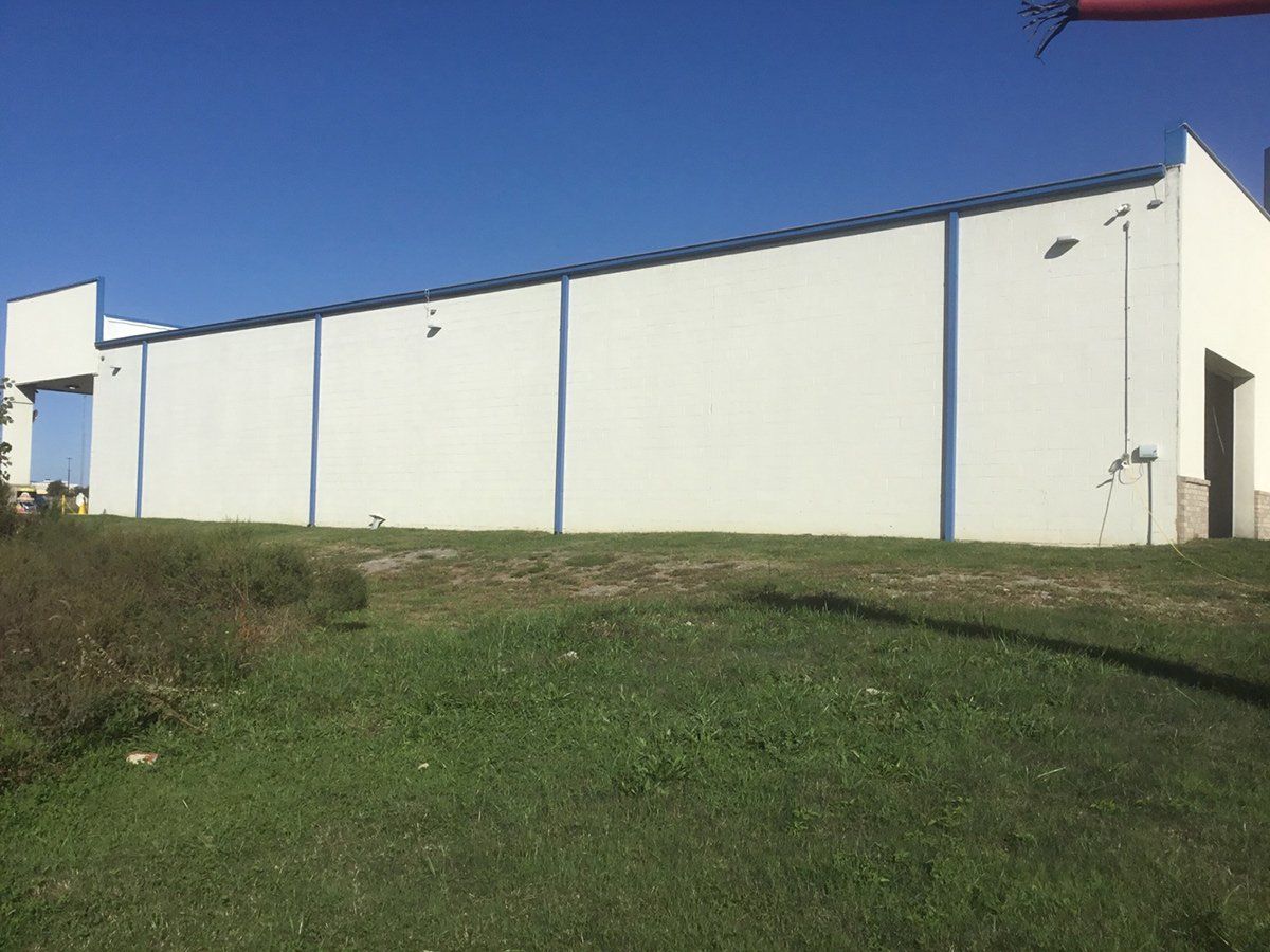 A large white building with blue trim is sitting in the middle of a grassy field.