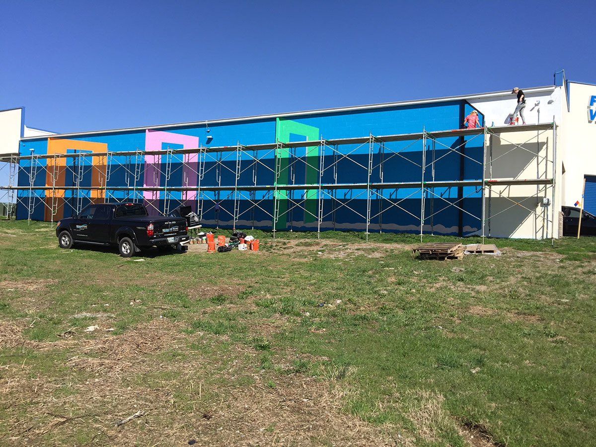 A car is parked in front of a building that is being painted.
