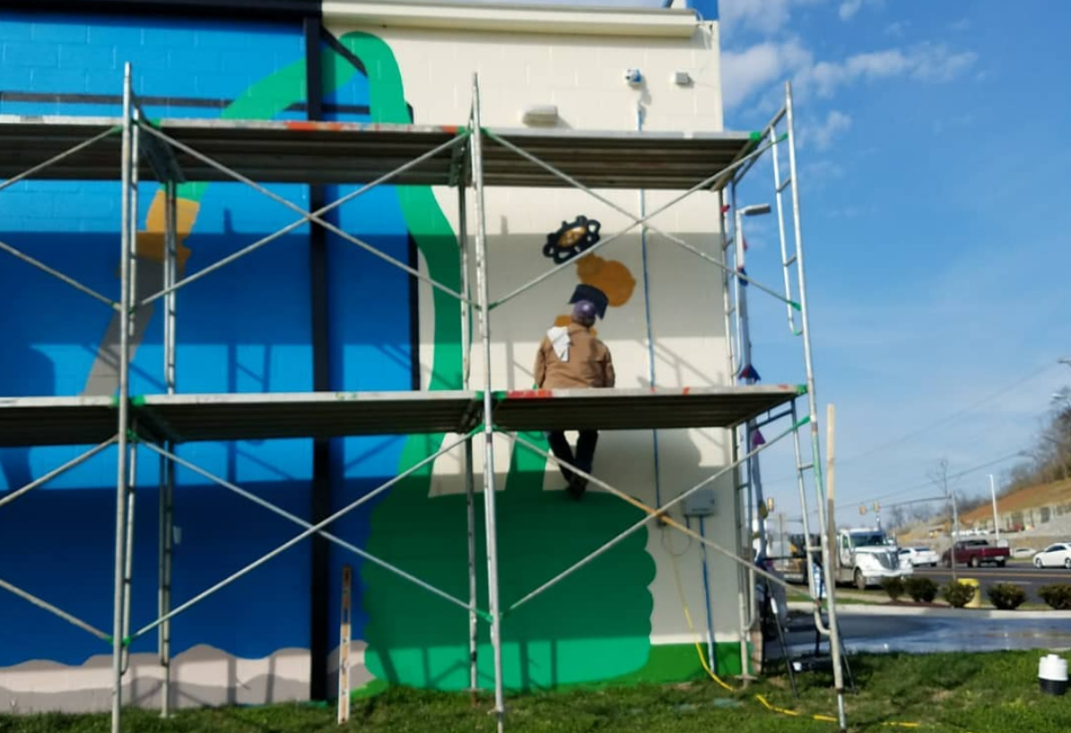 A man is painting a mural on the side of a building.