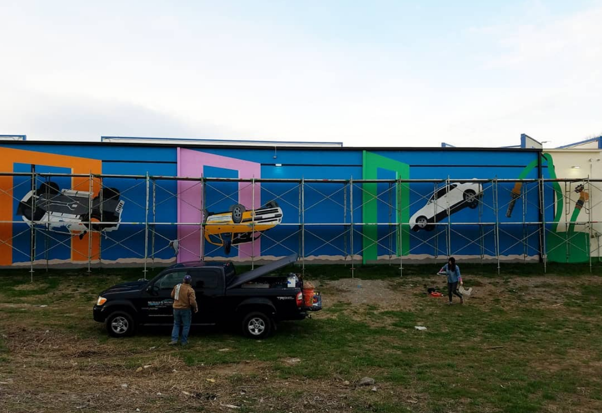A car is parked in front of a wall with cars painted on it