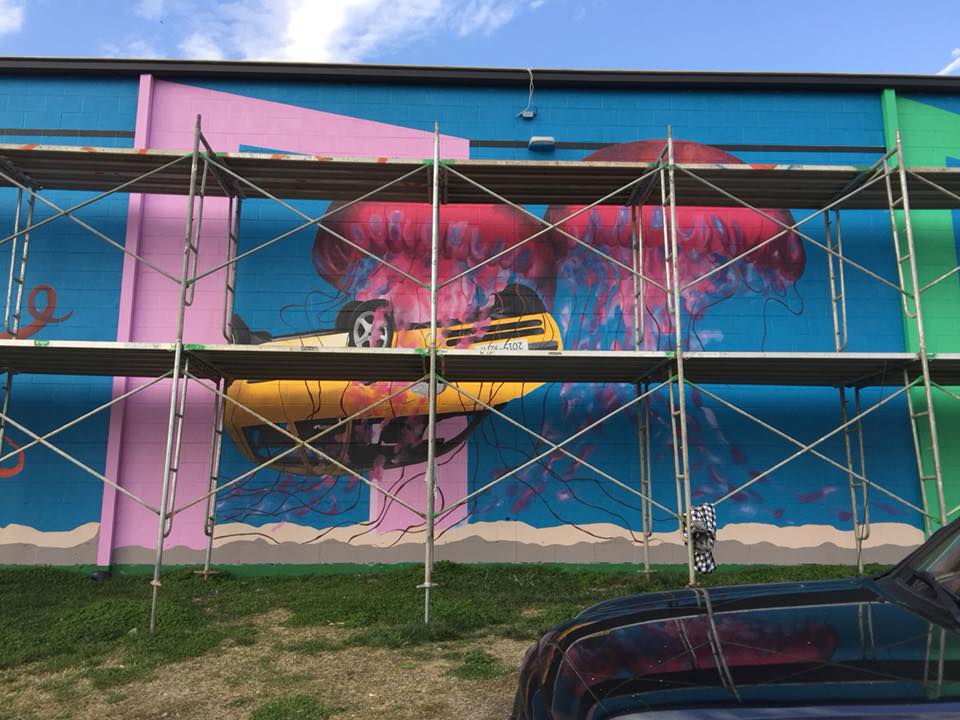 A large mural is being painted on the side of a building.