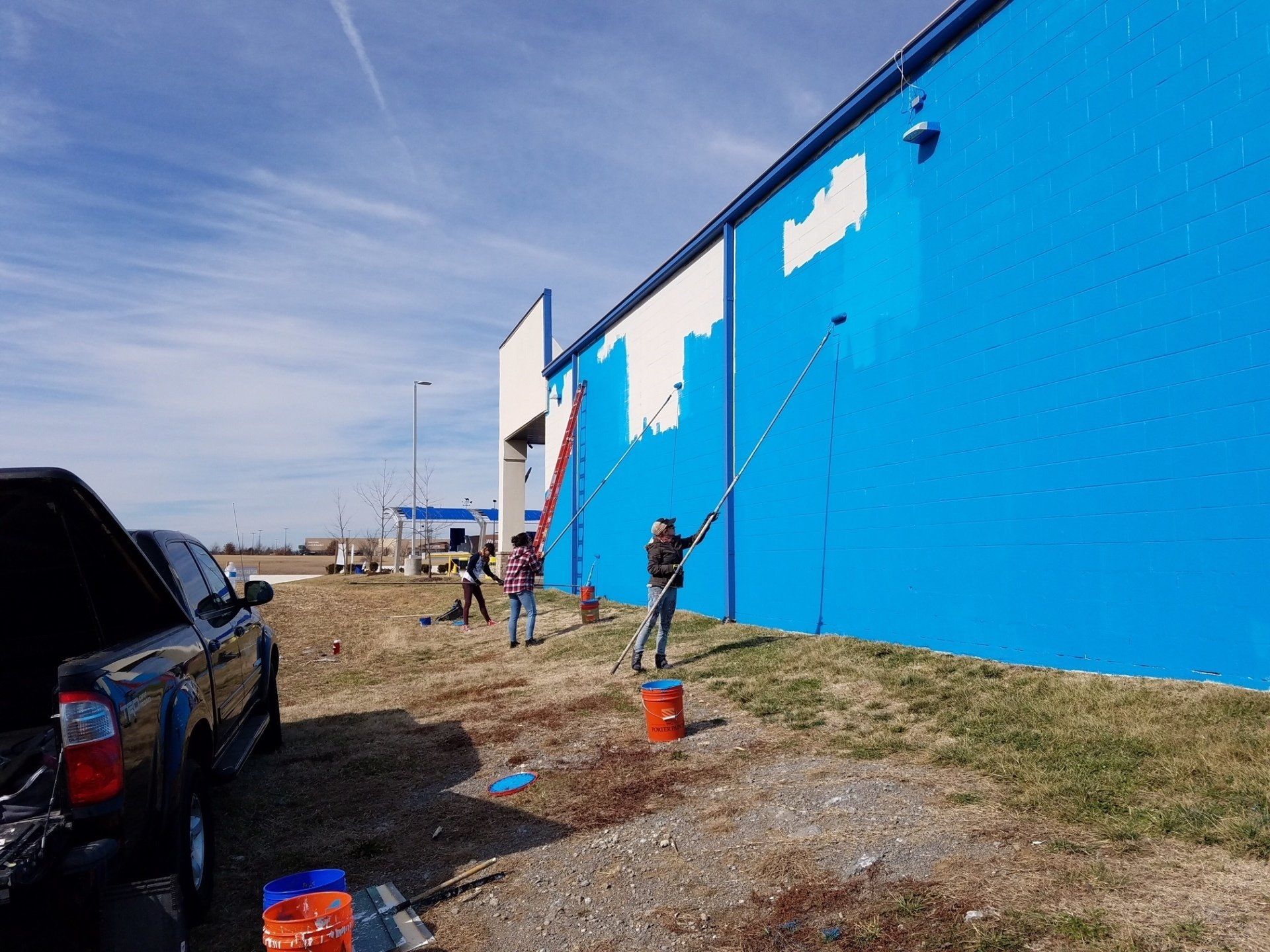 A group of people are painting a blue building with white paint.