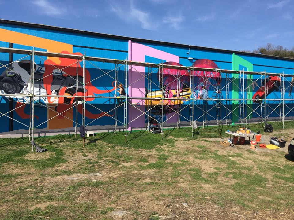 A large mural is being painted on the side of a building.