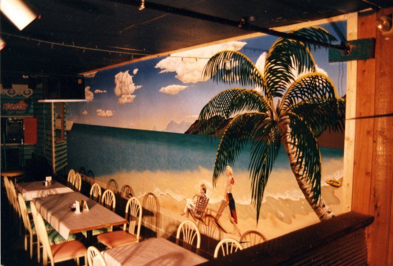 A restaurant with tables and chairs and a painting of a beach on the wall