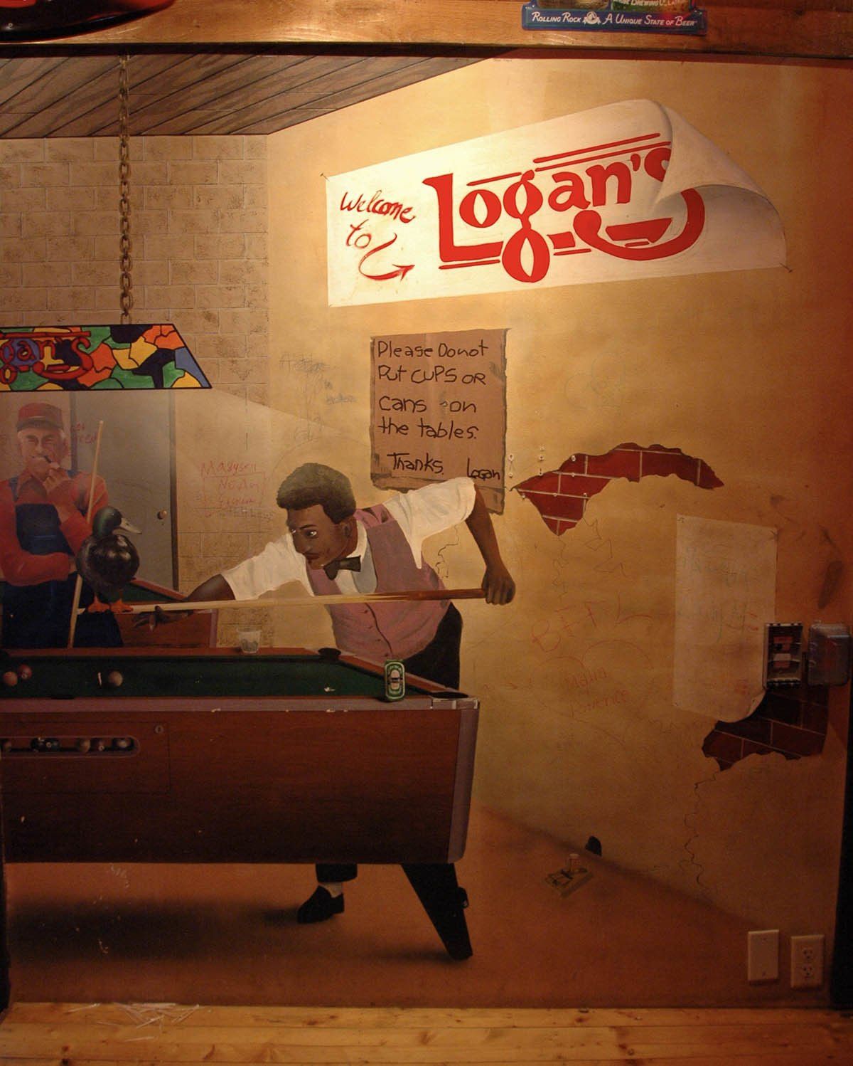 A man is playing pool in front of a sign that says logan 's
