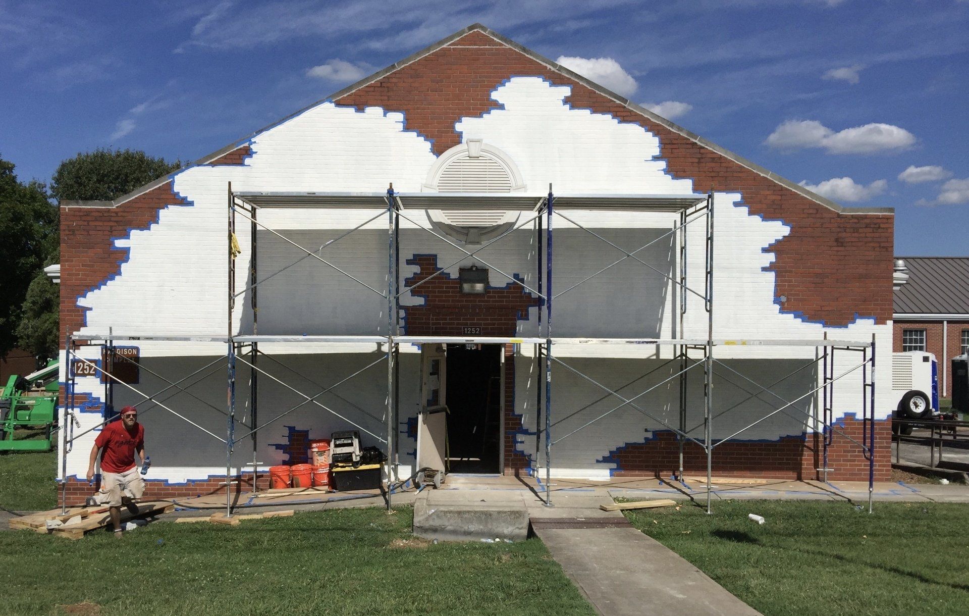 A brick building is being painted white with scaffolding around it.