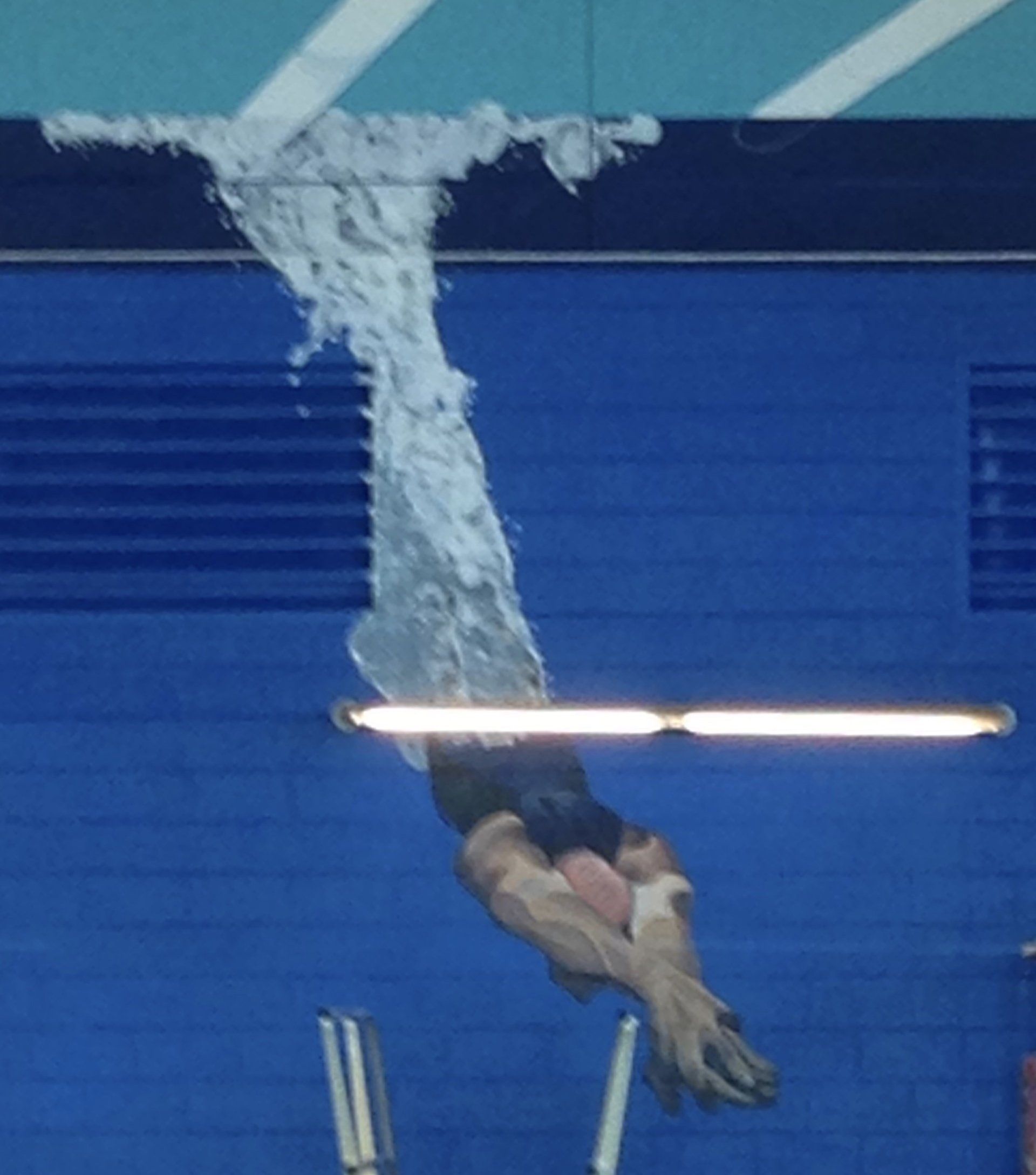 A person is diving into a pool with a blue wall in the background