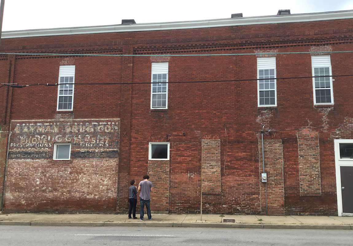 Two people are standing on the sidewalk in front of a brick building.