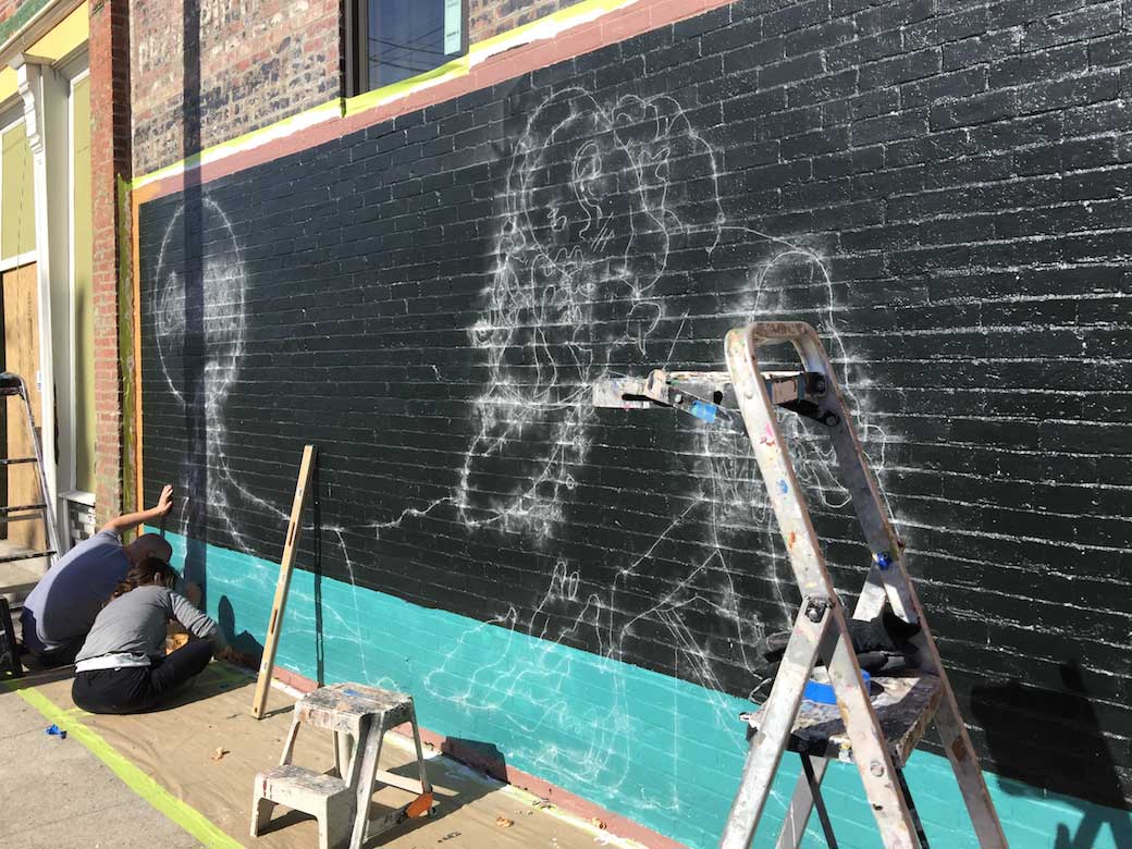 A group of people are painting a mural on the side of a building.