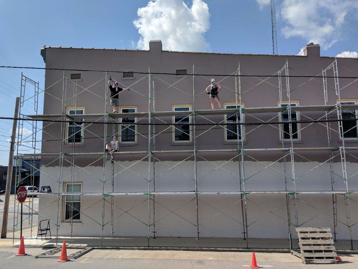 A building is being painted with scaffolding on the side of it.