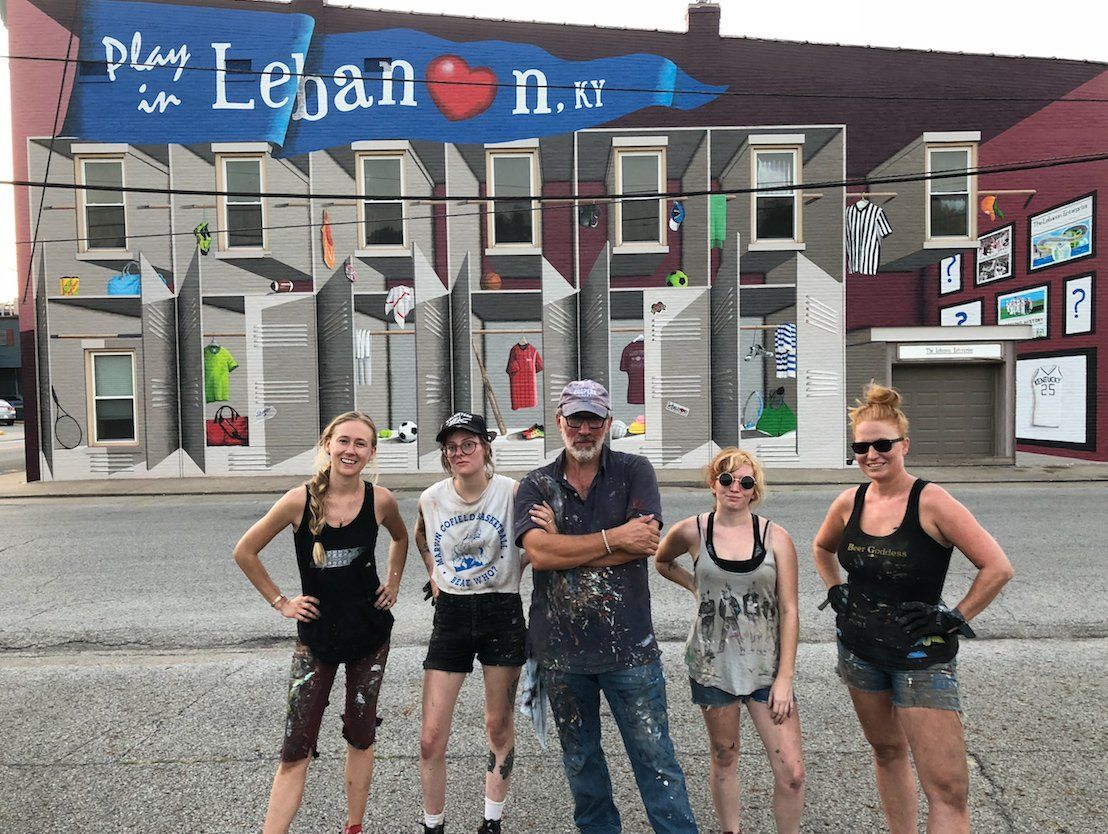 A group of people standing in front of a building with a mural on it.