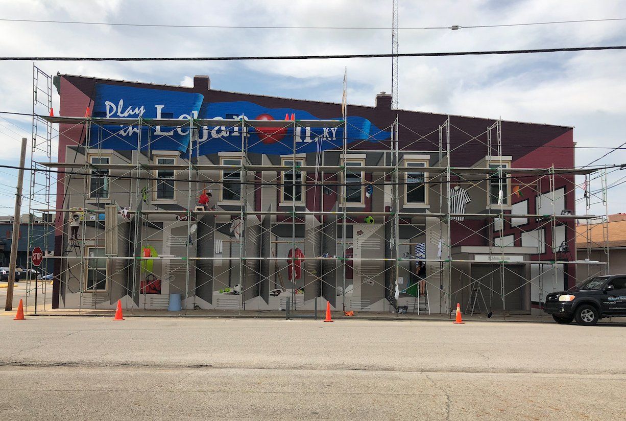 A large mural is being painted on the side of a building.