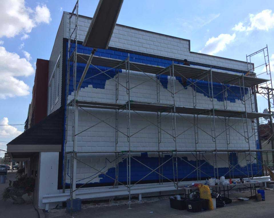 A building is being painted blue and white with scaffolding.