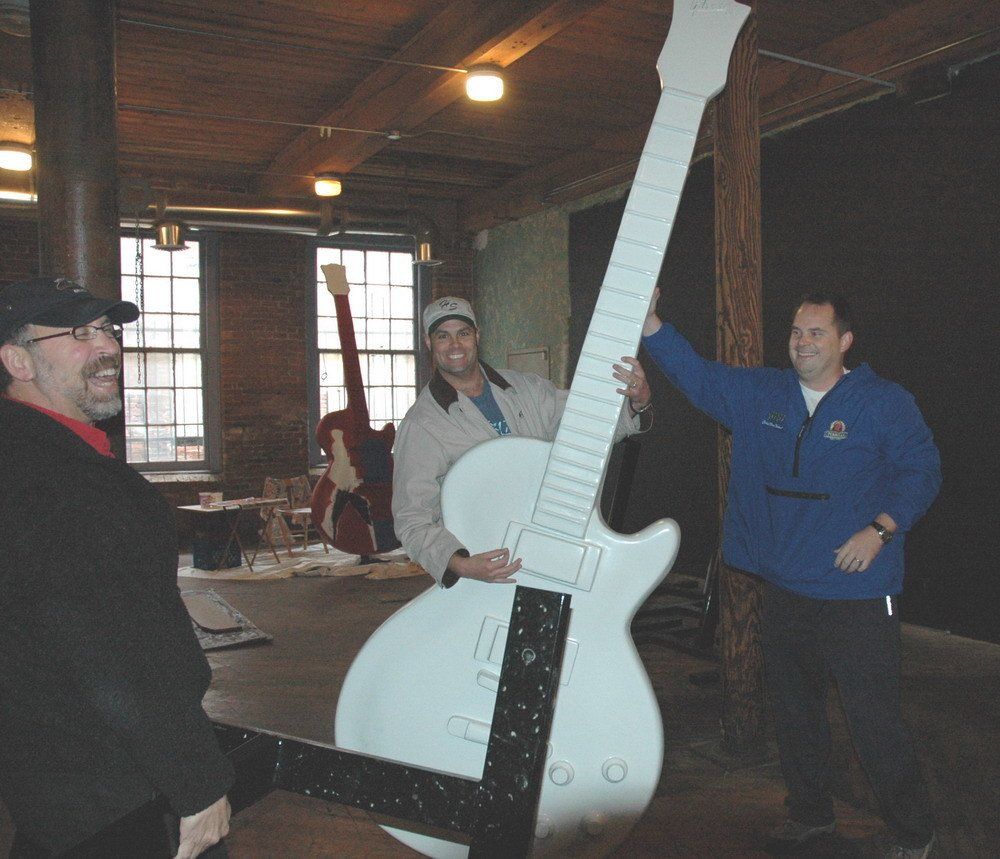 A man in a blue jacket is holding a large white guitar