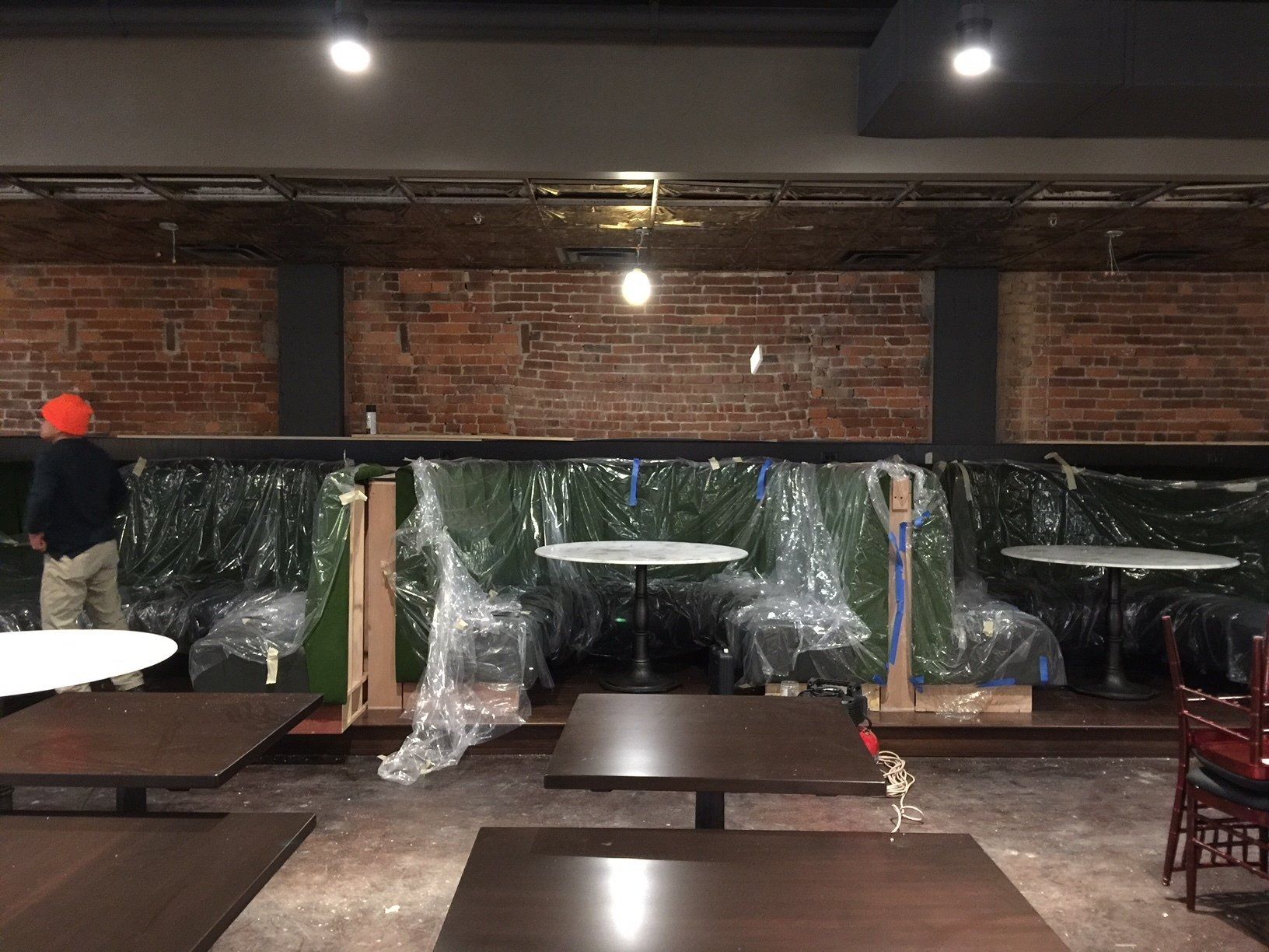 A man is standing in an empty restaurant with tables and chairs covered in plastic.