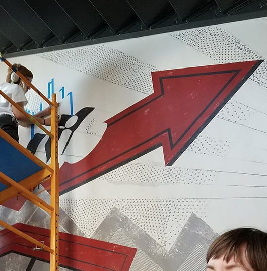 A man is standing on a ladder in front of a large arrow on a wall