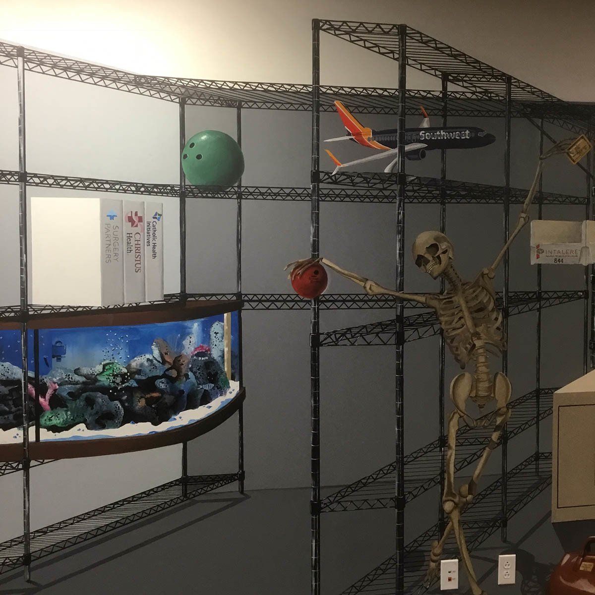 A skeleton is holding an apple in front of a fish tank
