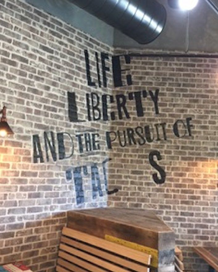 A brick wall with the words life liberty and the pursuit of tall stenciled on it