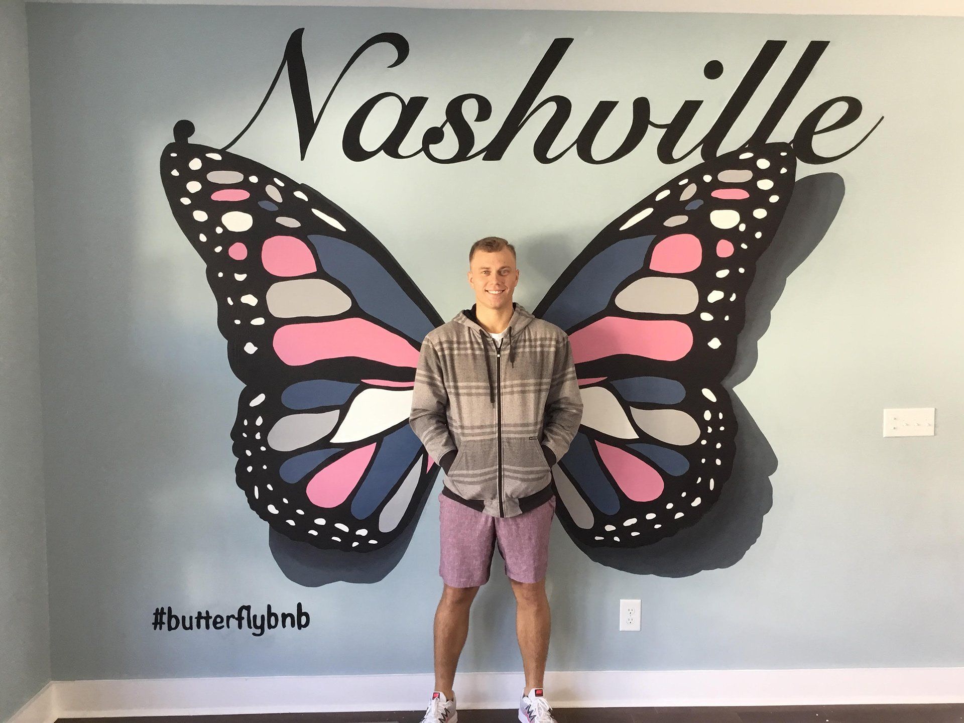 A man is standing in front of a mural of a butterfly and the word nashville