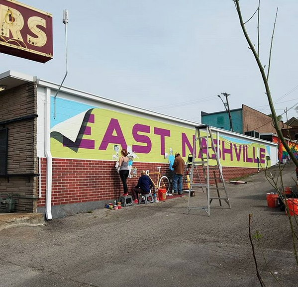 People are painting a mural on the side of a building that says east nashville